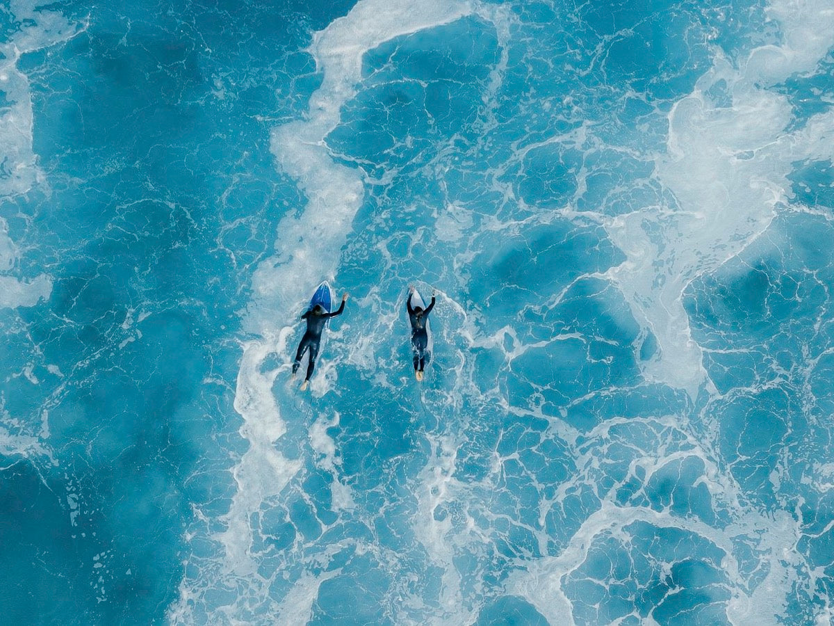 Two surfers paddling through turquoise waves – End of Summer Sale
