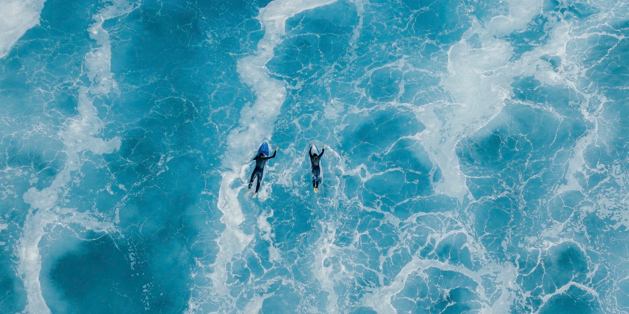 Two surfers paddling through turquoise waves – End of Summer Sale